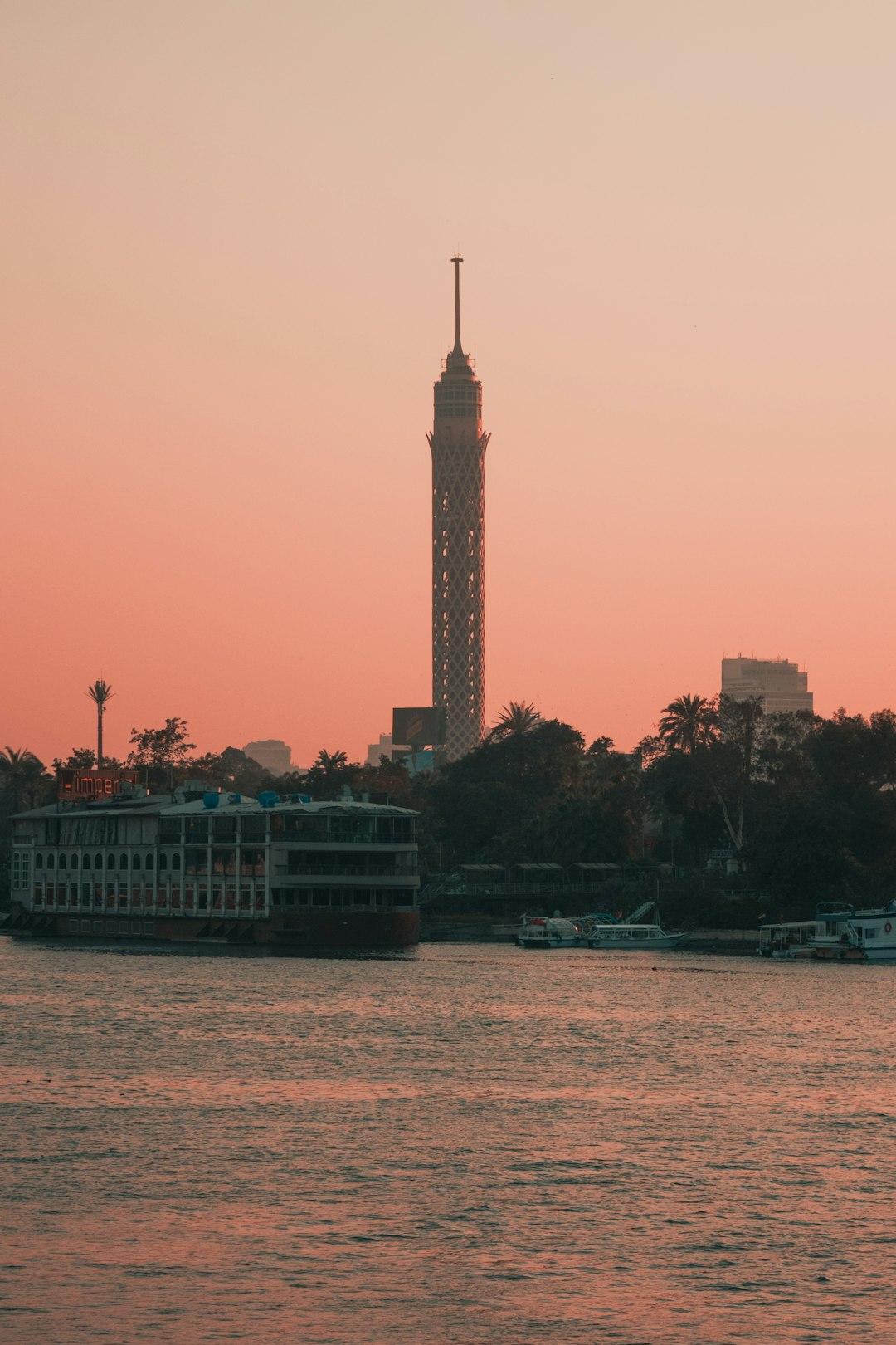 Cairo Tower rising above the Nile at sunset with moored riverboats and a pink-orange sky
