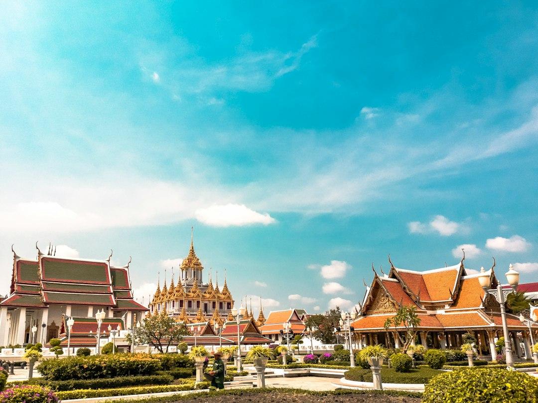 Thai temple complex with golden spires and orange-roofed pavilions surrounded by manicured gardens under a bright blue sky in Bangkok