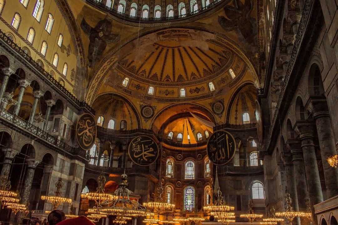 Golden domed interior of Hagia Sophia with large Arabic calligraphy medallions and glowing chandeliers, Istanbul