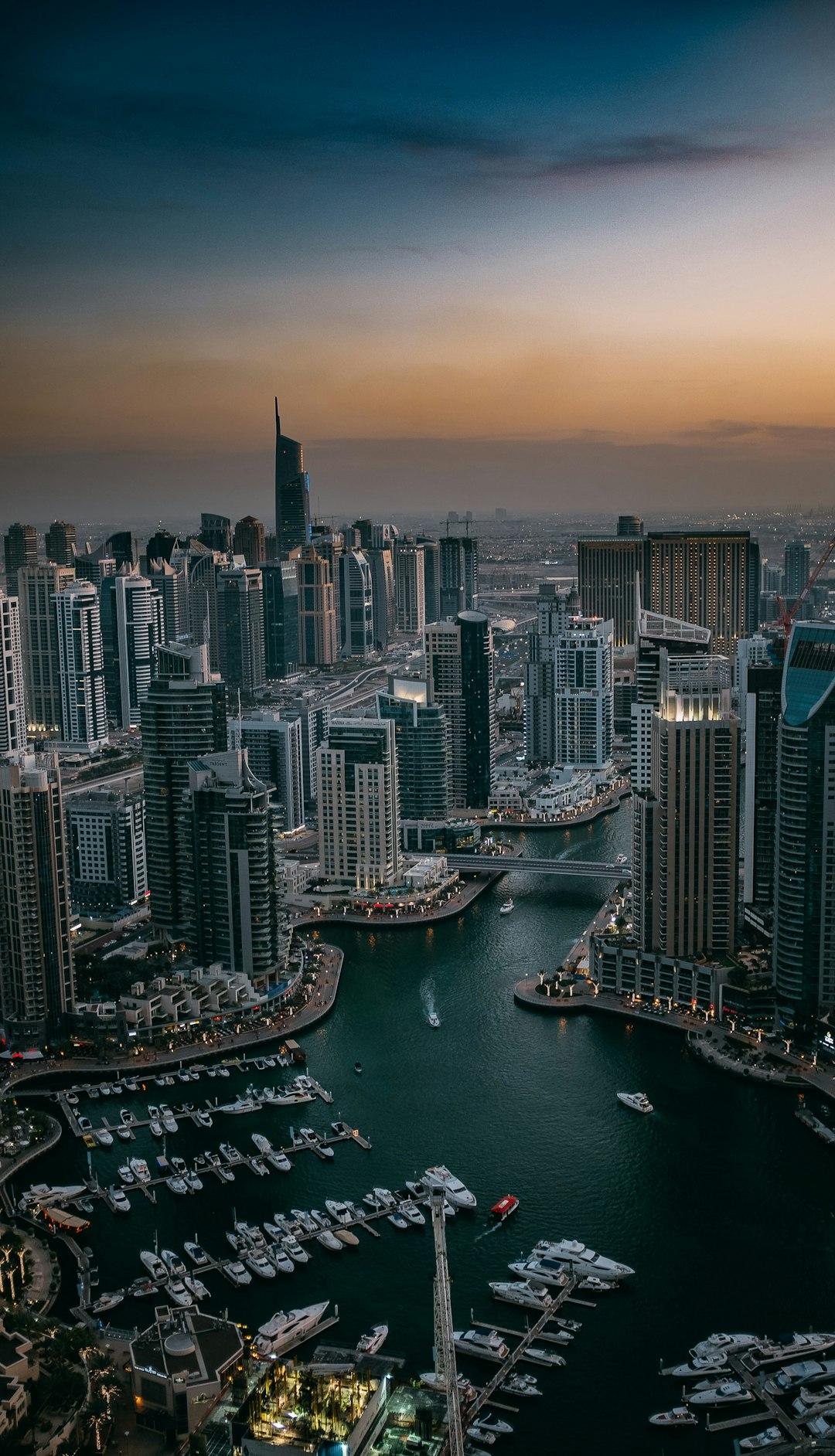 Aerial view of Dubai Marina at dusk, with luxury yachts, a waterway canal, and glittering skyscrapers under a golden sunset sky