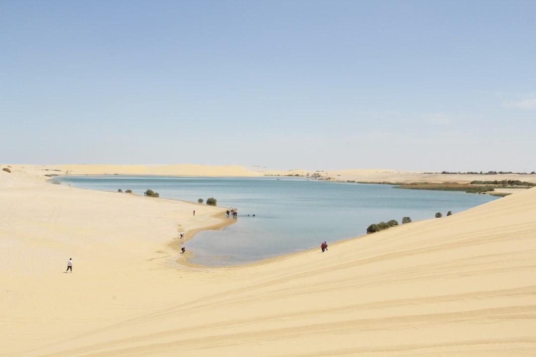 Turquoise desert lake nestled among pale sand dunes at Siwa Oasis, Egypt, with visitors walking along the sandy shore
