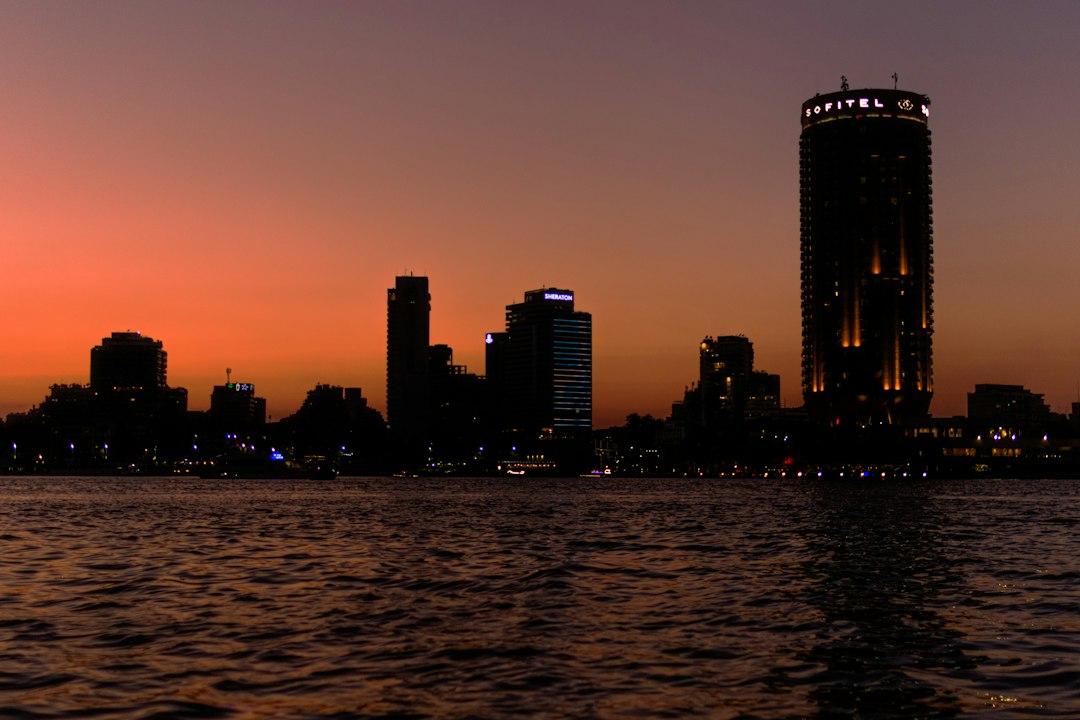 Cairo skyline at sunset with Sofitel and Sheraton towers silhouetted against an orange sky, reflected on the Nile