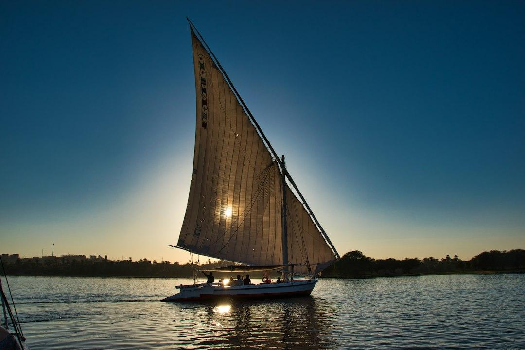 Traditional felucca sailboat gliding on the Nile River at sunset near Aswan, with sun shining through white sail