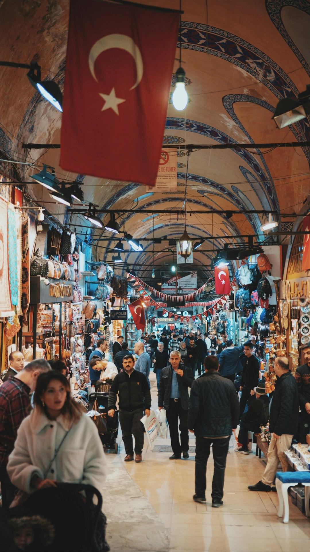 Crowded Grand Bazaar passage in Istanbul with Turkish flags, arched ceilings, and shops selling bags and souvenirs