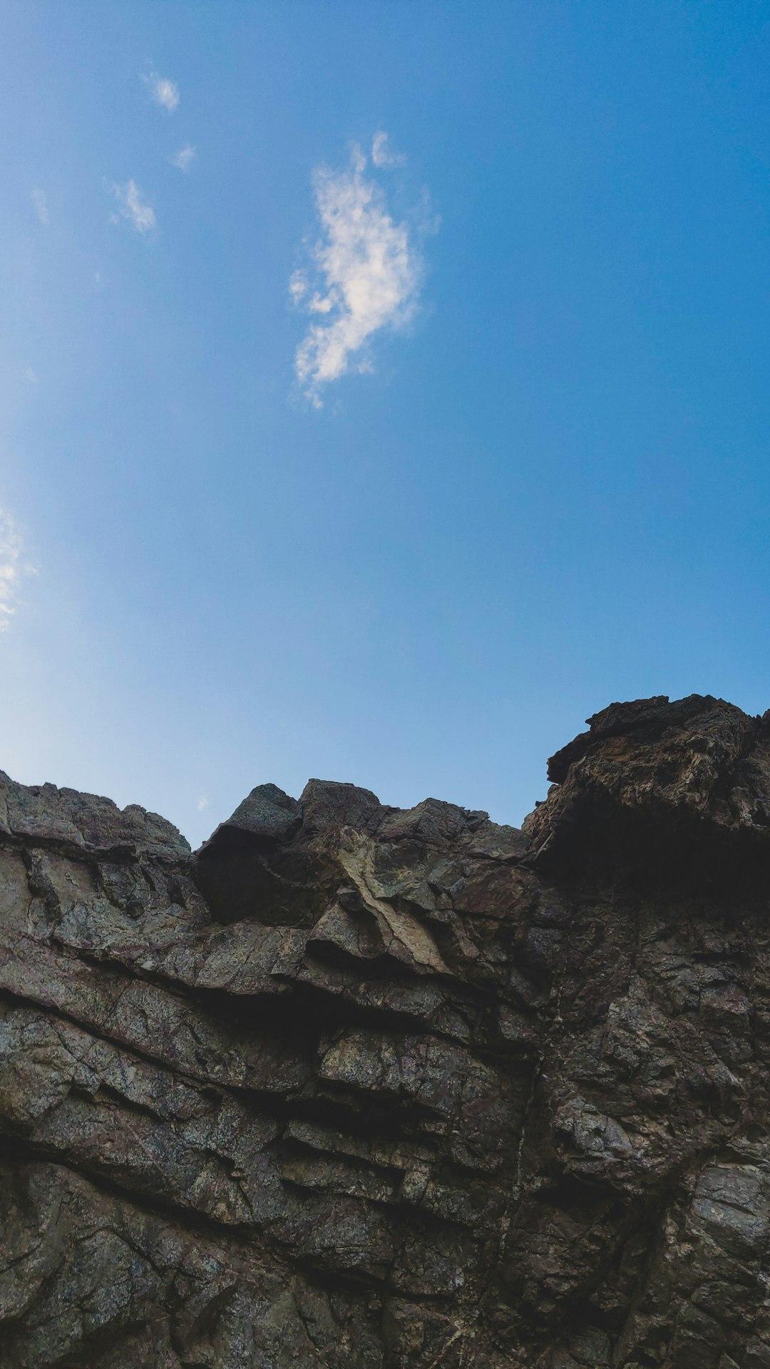 Low-angle view of jagged rocky cliffs against a clear blue sky with a single wispy cloud in Dahab, Egypt