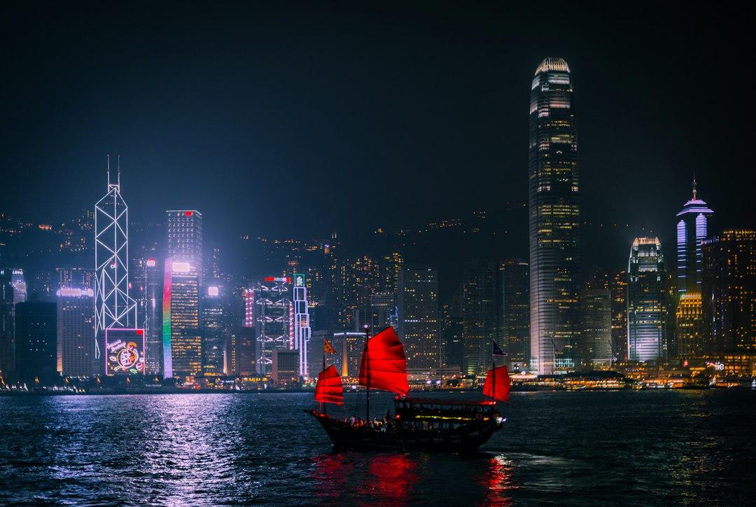 Traditional red-sailed junk boat crossing Victoria Harbour at night with Hong Kong's illuminated skyline behind