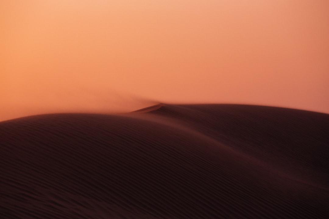 Dark rippled sand dune ridge shrouded in blowing dust under a hazy orange sky in Egypt's Eastern Desert