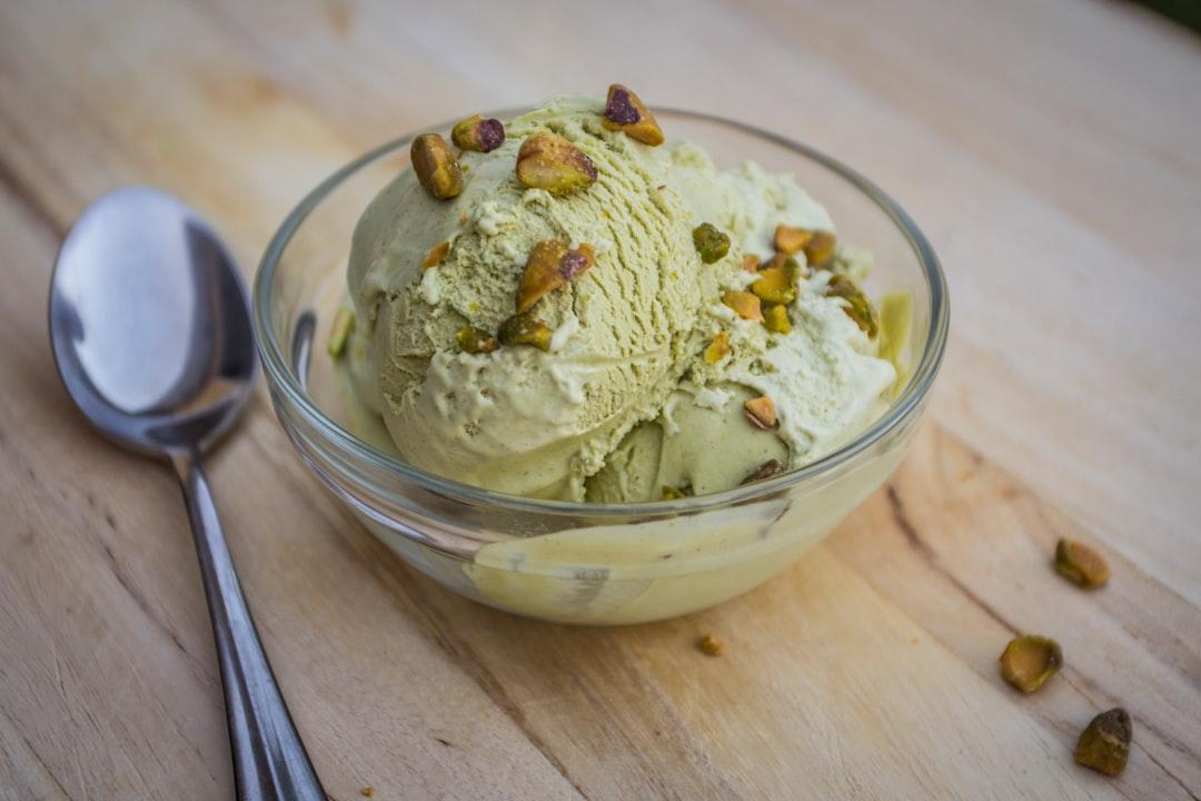 A vibrant scoop of pistachio gelato held against Santorini's whitewashed caldera-edge walls at golden hour