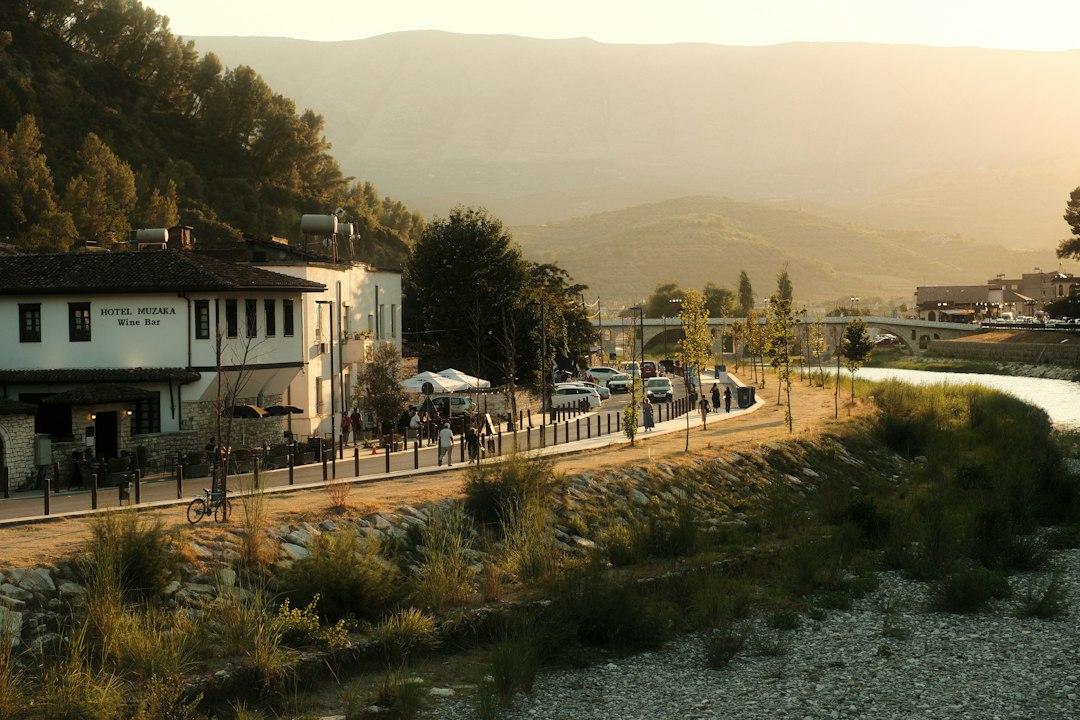 Hotel Muzaka Wine Bar along Berat riverfront at golden hour, with stone bridge and mountains in background, Albania