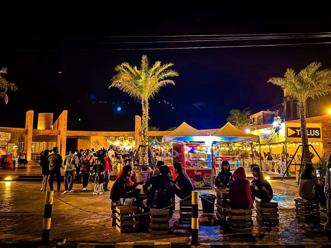 Busy outdoor night market at Soho Square Sharm El Sheikh with palm trees, food stalls, and families seated at wooden tables