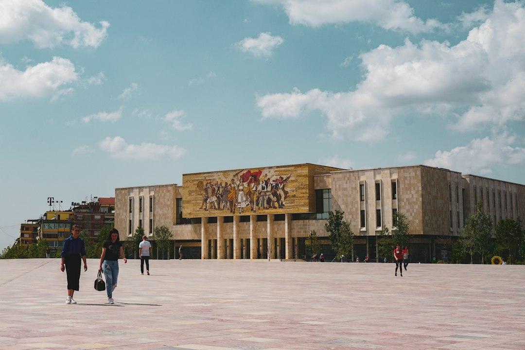 Skanderbeg Square in Tirana with the National History Museum's colorful mosaic facade and pedestrians on sunny day