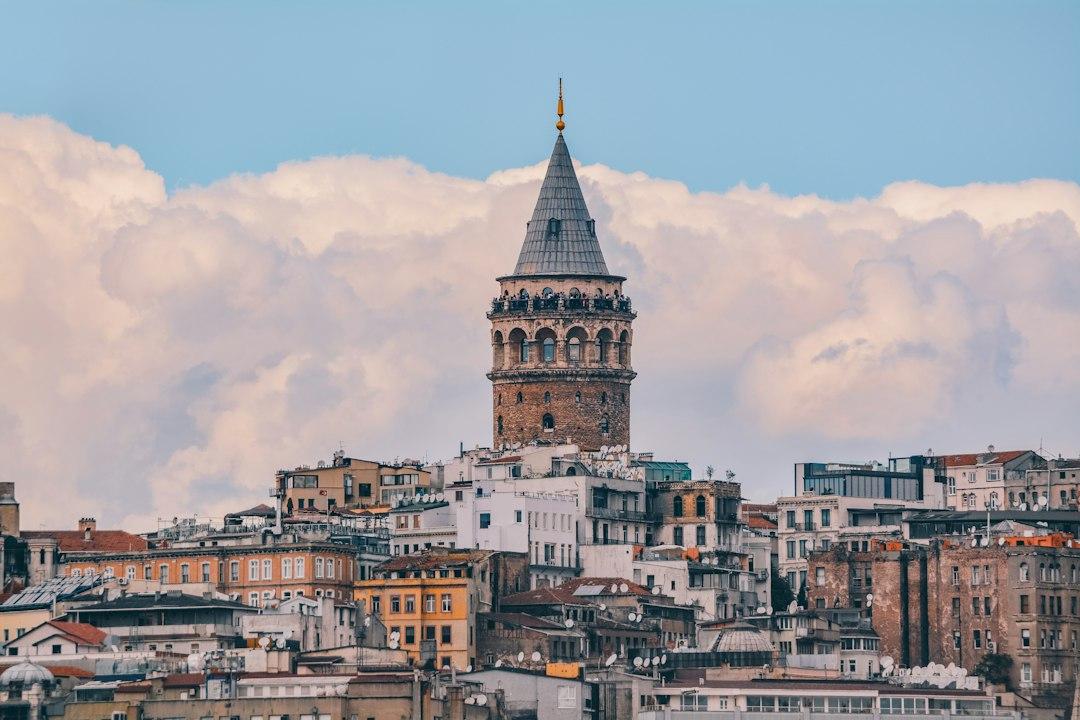 Galata Tower rising above dense Istanbul rooftops in Beyoglu district under a cloudy blue sky