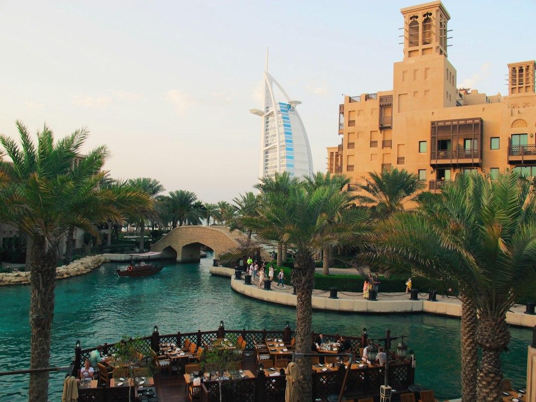 Outdoor waterfront dining terrace at Madinat Jumeirah with palm trees, turquoise canals, and Burj Al Arab in background