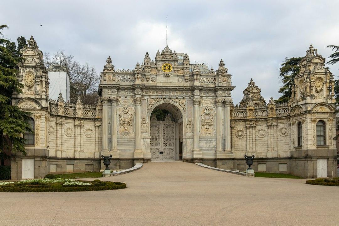 Ornate baroque facade and grand arched gate of Dolmabahçe Palace in Istanbul, Turkey, under a cloudy sky