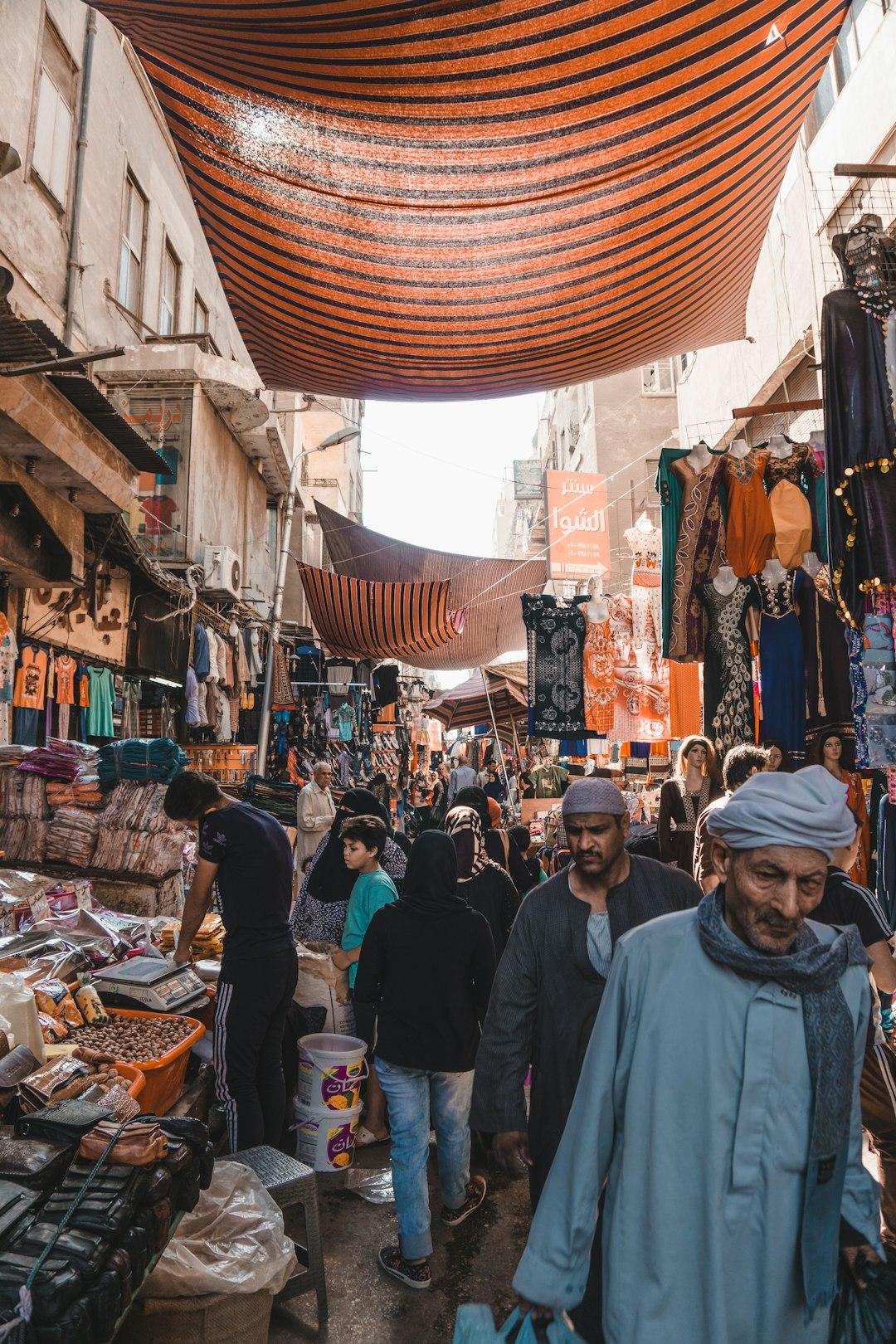 Crowded Cairo street market in Shubra with orange striped canopies, clothing stalls, and locals shopping