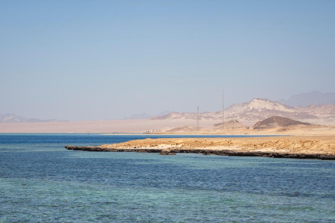 Turquoise Red Sea waters beside a rocky desert shoreline with arid mountains and radio towers in Hurghada, Egypt