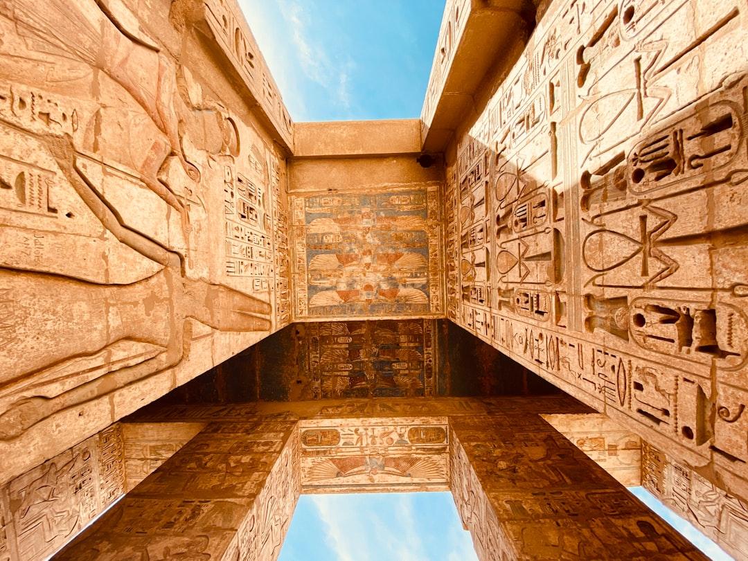 Upward view of ancient Egyptian temple columns densely carved with hieroglyphics and colorful painted reliefs under a blue sky