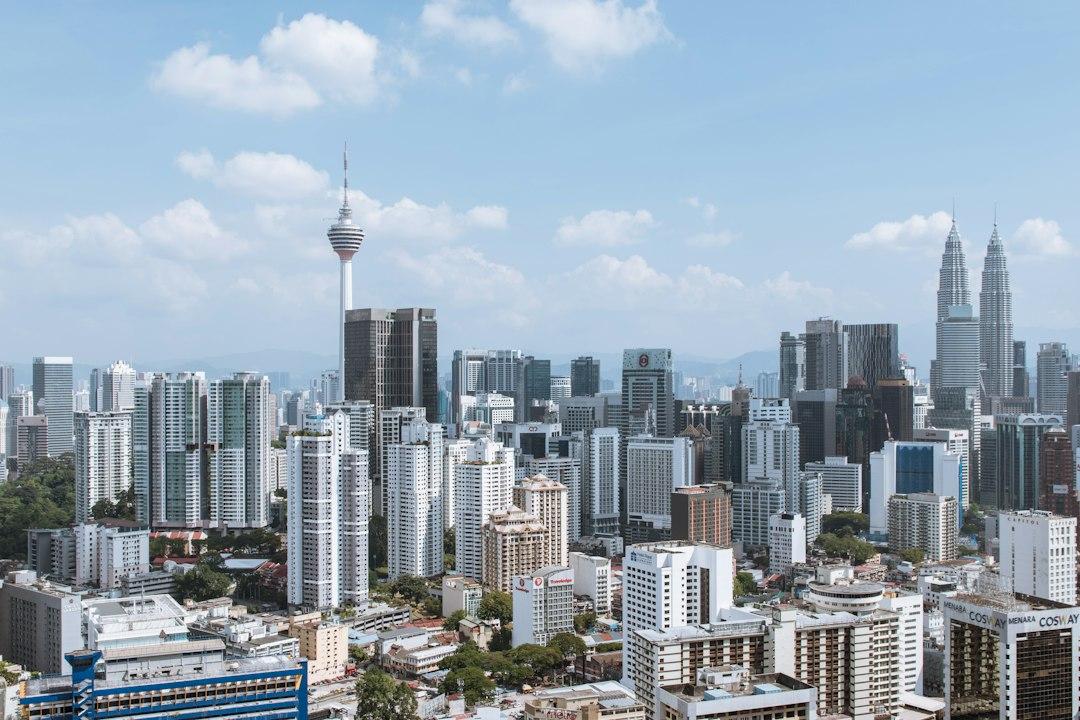 Kuala Lumpur skyline with KL Tower and Petronas Twin Towers rising above dense city skyscrapers under a blue sky
