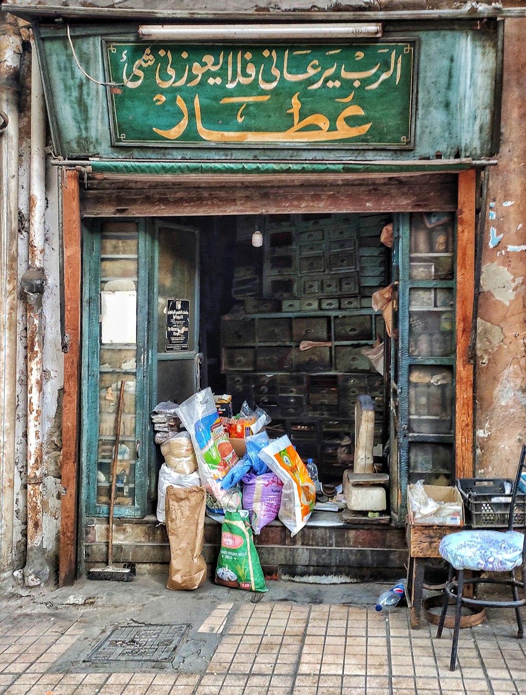 Weathered Arabic apothecary shop in Downtown Cairo with green signage, wooden drawers, and goods piled at entrance