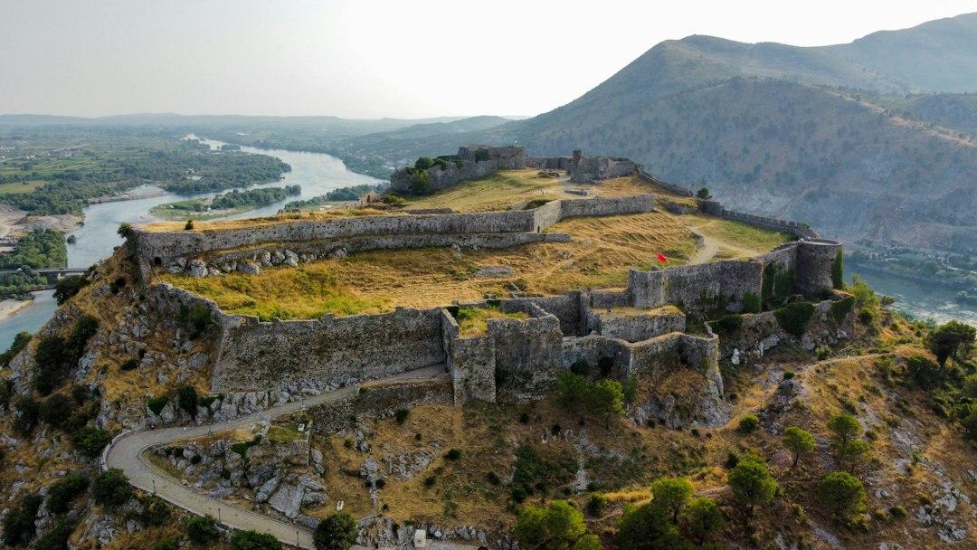 Aerial view of Gjirokaster Castle perched on a rocky hilltop in Albania, with stone walls and a river winding through the valley below