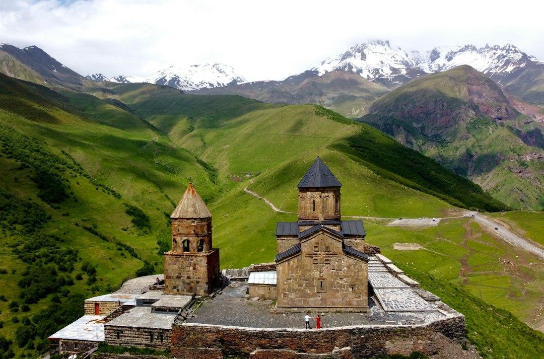 Gergeti Trinity Church perched on a hilltop with lush green Caucasus valleys and snow-capped mountains in Kazbegi, Georgia