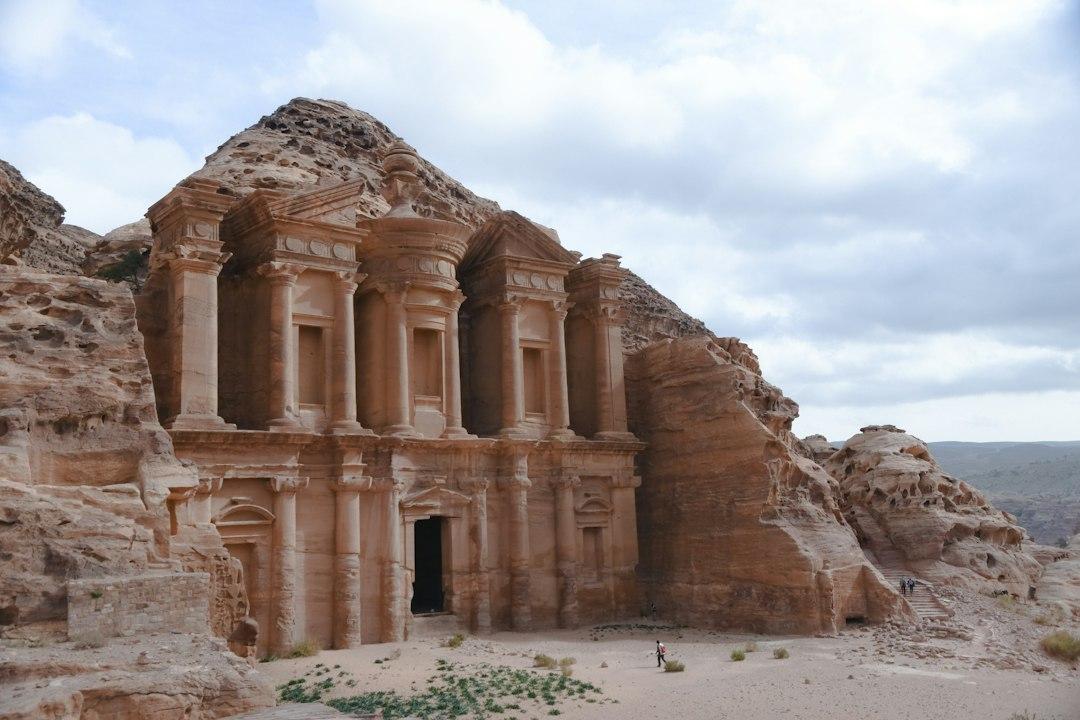Ad Deir Monastery carved into rose-red sandstone cliffs in Petra, Jordan, with a lone visitor standing below