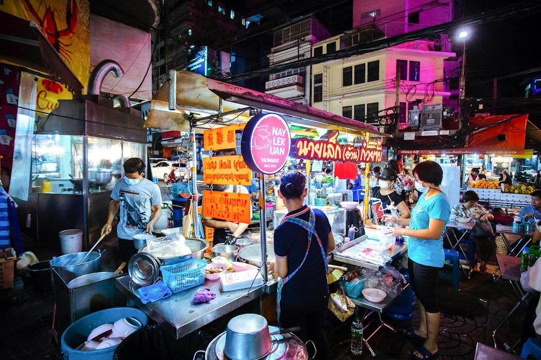Busy Bangkok street food stalls at night with neon signs, vendors cooking noodles at Nay Lek Uan in Yaowarat Chinatown