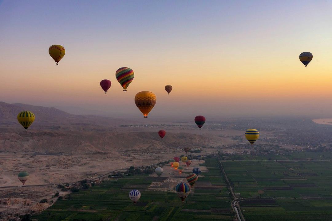 Dozens of colorful hot air balloons floating over the Nile Valley and desert cliffs of Luxor at sunrise