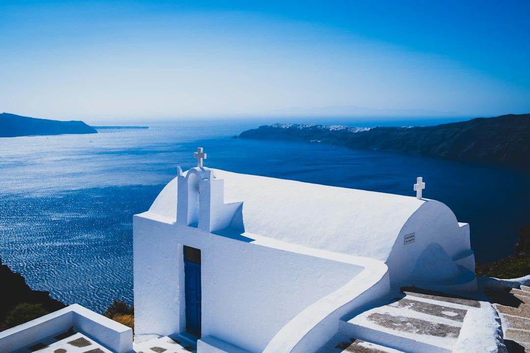 Whitewashed Greek Orthodox chapel with blue door and twin crosses overlooking Santorini caldera and Aegean Sea