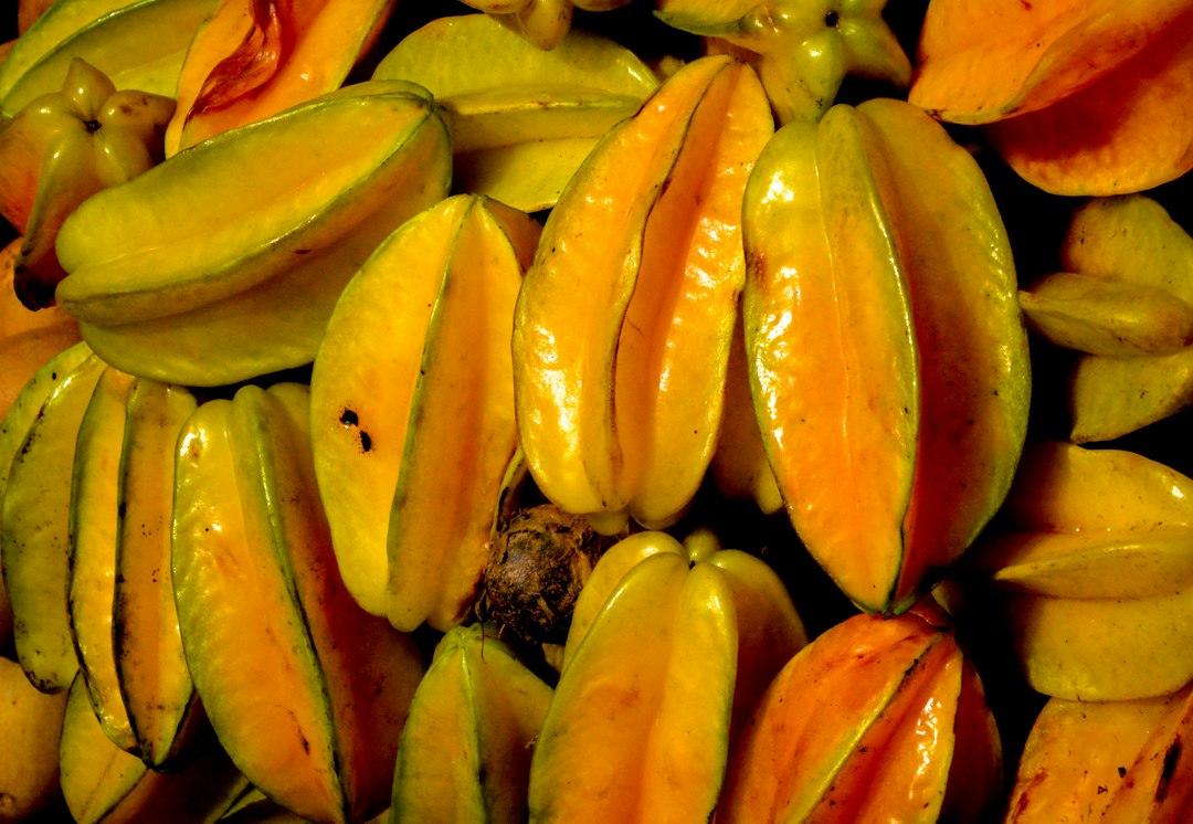 Pile of ripe starfruit with glossy yellow-orange skin and distinct ribbed edges at a Bali beach fruit cart